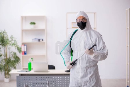 Téléchargez les photos : Jeune entrepreneur désinfectant le bureau pendant la pandémie - en image libre de droit