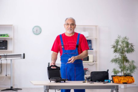 Photo for Old male repairman repairing sandwich maker at workshop - Royalty Free Image