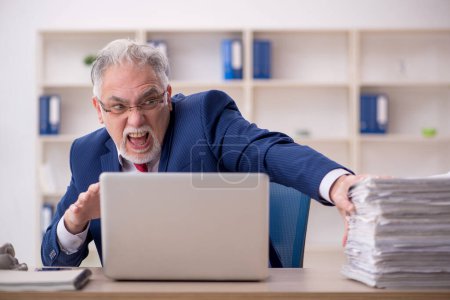 Foto de Old employee unhappy with excessive work at workplace - Imagen libre de derechos