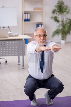 Photo for Old male employee doing sport exercises during break - Royalty Free Image