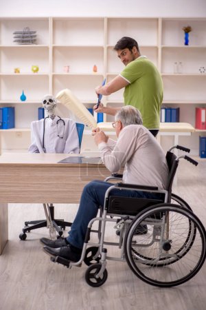 Photo for Old male patient in wheel-chair visiting skeleton doctor - Royalty Free Image