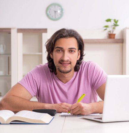 Téléchargez les photos : Le jeune étudiant masculin se prépare aux examens à la maison - en image libre de droit
