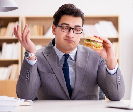 Foto de El hambriento empresario divertido comiendo sándwich de comida chatarra - Imagen libre de derechos