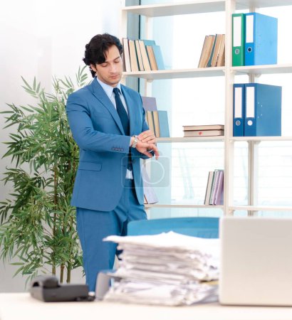 Foto de El joven y apuesto empleado masculino con demasiado trabajo en la oficina - Imagen libre de derechos