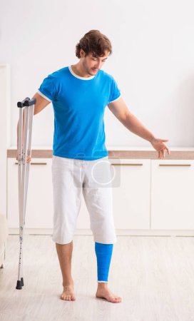 Foto de La pierna herido joven con muletas en casa - Imagen libre de derechos