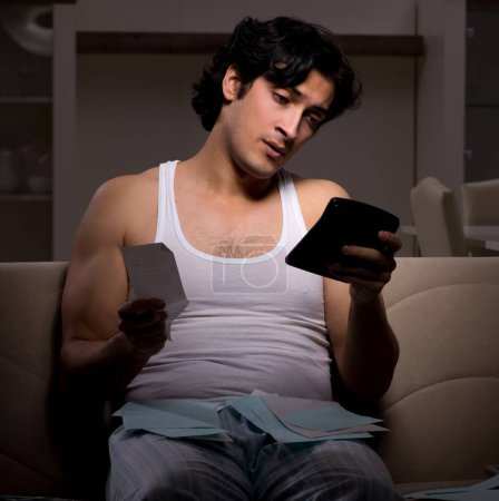 Téléchargez les photos : Le jeune homme calcule les dépenses nuit à la maison - en image libre de droit