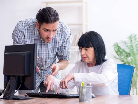Photo for Young male employee explaining to old female colleague how to use computer - Royalty Free Image