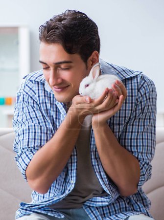 Téléchargez les photos : Le jeune homme jouant avec le lapin animal à la maison - en image libre de droit