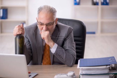 Foto de Viejo empleado bebiendo alcohol en el lugar de trabajo - Imagen libre de derechos