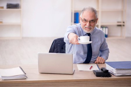 Téléchargez les photos : Old employee drinking tea at workplace - en image libre de droit