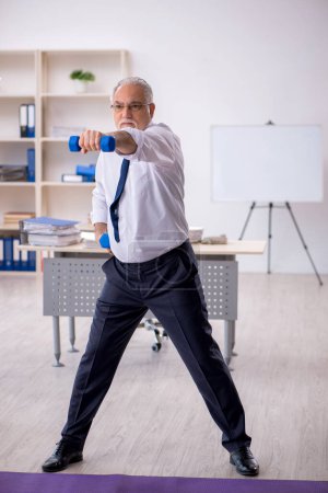 Foto de Viejo empleado masculino haciendo ejercicios deportivos durante el descanso - Imagen libre de derechos
