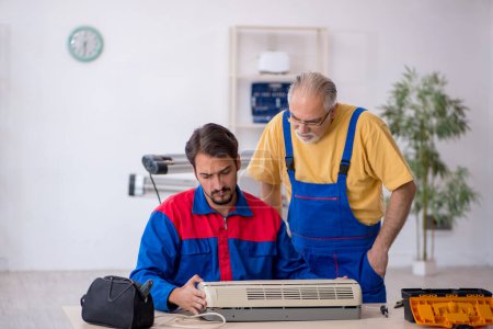 Téléchargez les photos : Deux réparateurs réparant le climatiseur à l'atelier - en image libre de droit