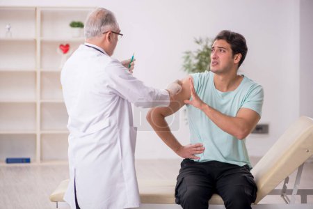 Téléchargez les photos : Jeune patient visitant un vieux médecin masculin dans le concept de vaccination - en image libre de droit