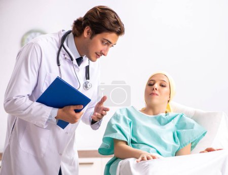 Foto de El joven y guapo doctor visitando a una paciente de oncología femenina - Imagen libre de derechos