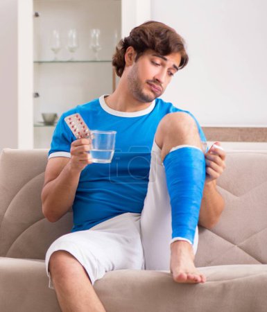 Téléchargez les photos : La jambe blessée jeune homme sur le canapé - en image libre de droit