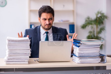 Foto de Joven empleado masculino y demasiado trabajo en la oficina - Imagen libre de derechos