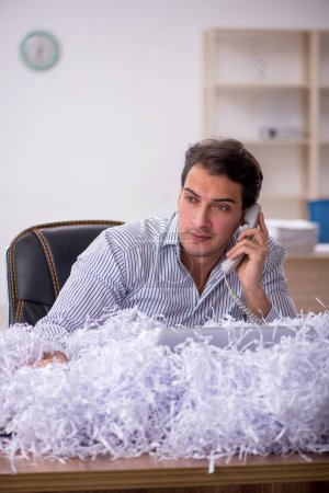 Téléchargez les photos : Jeune homme d'affaires employé et beaucoup de papiers coupés sur le lieu de travail - en image libre de droit