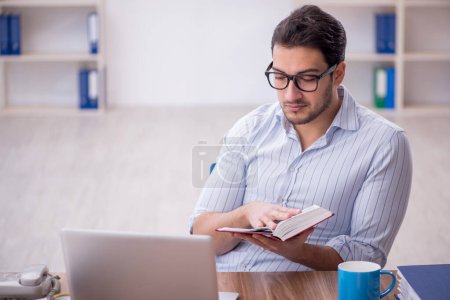 Photo for Young businessman employee reading book at workplace - Royalty Free Image