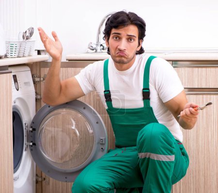 Téléchargez les photos : Le jeune entrepreneur réparer la machine à laver dans la cuisine - en image libre de droit