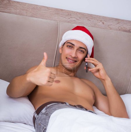 Téléchargez les photos : L'homme sexy dans le lit portant un chapeau de Père Noël dans le concept de Noël - en image libre de droit