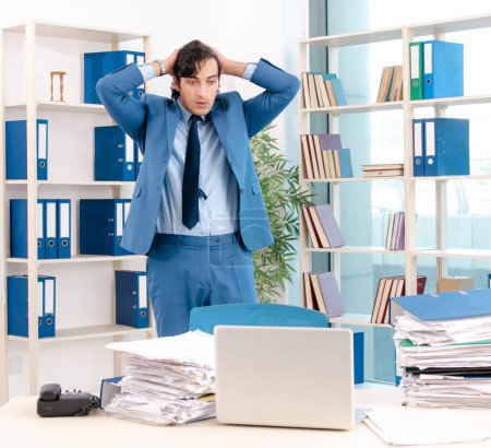 Foto de El joven y apuesto empleado masculino con demasiado trabajo en la oficina - Imagen libre de derechos