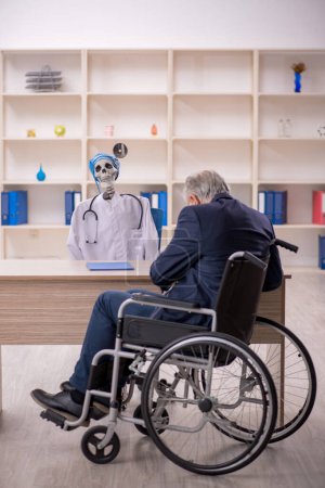 Foto de Viejo paciente masculino en silla de ruedas visitando al doctor diablo - Imagen libre de derechos