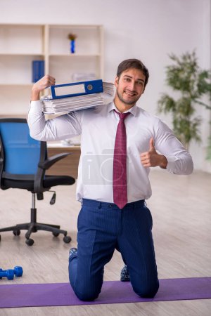 Photo for Young employee doing sport exercises during break - Royalty Free Image