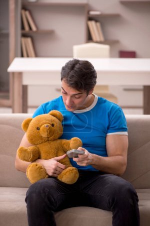 Téléchargez les photos : Jeune homme assis avec jouet ours à la maison - en image libre de droit