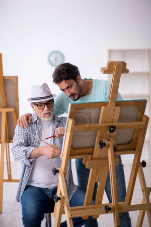 Foto de Viejo pintor masculino enseñando joven estudiante masculino en el estudio - Imagen libre de derechos