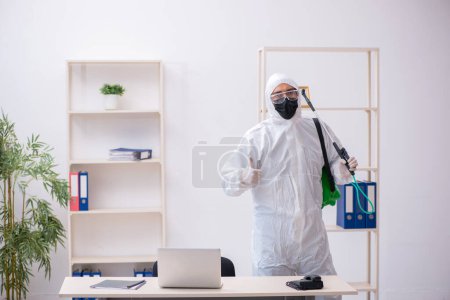 Foto de Joven contratista desinfectando oficina durante pandemia - Imagen libre de derechos