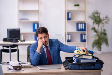 Photo for Young businessman employee preparing for trip at workplace - Royalty Free Image