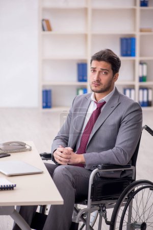 Foto de Young male employee in wheel-chair working at workplace - Imagen libre de derechos