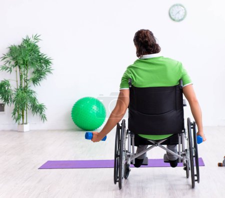 Photo for The young man in wheel-chair doing exercises indoors - Royalty Free Image