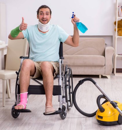 Téléchargez les photos : Le jeune homme en fauteuil roulant nettoie la maison - en image libre de droit