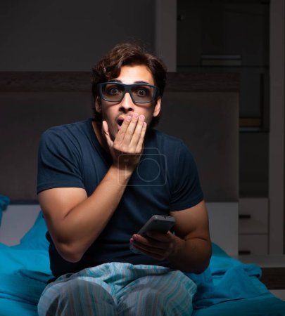 Téléchargez les photos : L'homme qui regarde la télé la nuit au lit - en image libre de droit