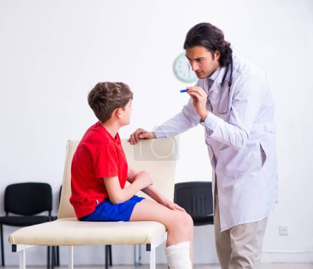 Foto de El niño lesionado pierna visitando al joven médico traumatólogo - Imagen libre de derechos