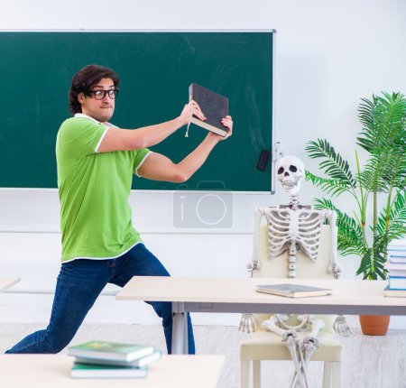 Téléchargez les photos : L'étudiant masculin drôle dans la salle de classe avec squelette - en image libre de droit