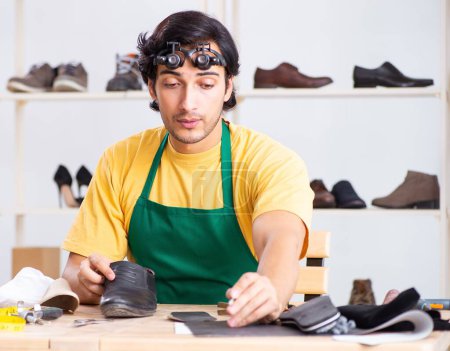 Téléchargez les photos : Le jeune homme réparant des chaussures en atelier - en image libre de droit