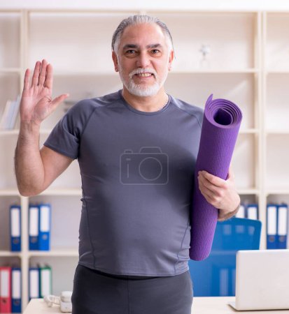 Foto de The white bearded old man employee doing exercises in the office - Imagen libre de derechos