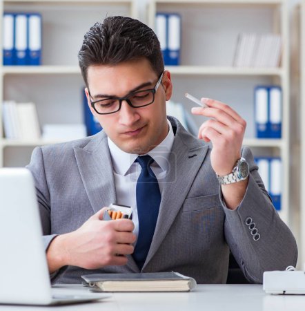 Téléchargez les photos : L'homme d'affaires fumant au bureau au travail - en image libre de droit