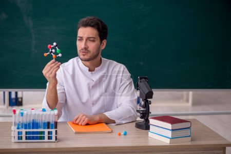 Téléchargez les photos : Jeune professeur de chimiste assis dans la salle de classe - en image libre de droit