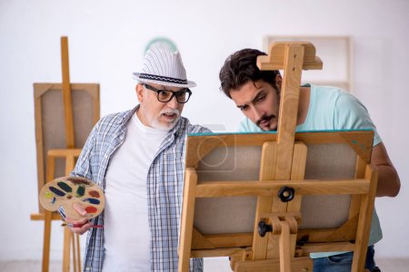 Téléchargez les photos : Vieux peintre enseignant jeune étudiant masculin au studio - en image libre de droit