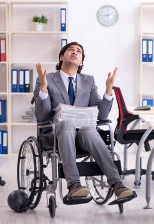 Foto de El joven empleado guapo en silla de ruedas que trabaja en la oficina - Imagen libre de derechos