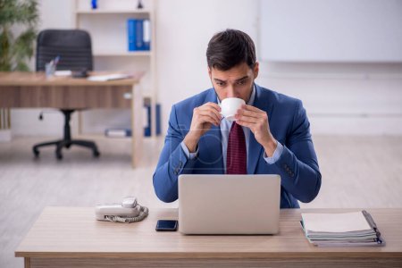 Foto de Empleado joven que bebe café en el lugar de trabajo - Imagen libre de derechos