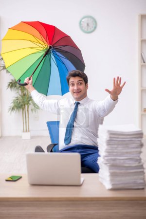 Foto de Young employee holding an umbrella at workplace - Imagen libre de derechos