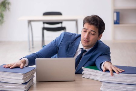 Photo for Young businessman employee and too much work at workplace - Royalty Free Image