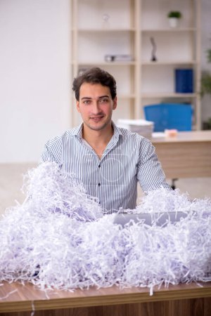 Foto de Empleado joven empresario y un montón de papeles cortados en el lugar de trabajo - Imagen libre de derechos