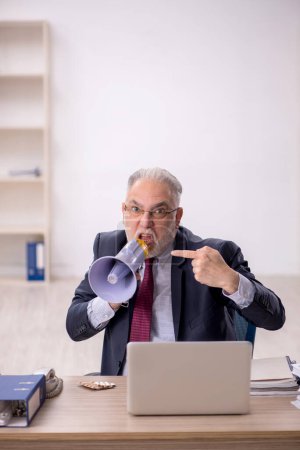 Photo for Old businessman employee holding magaphone in the office - Royalty Free Image