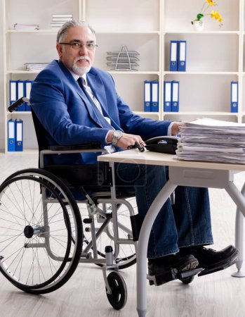 Téléchargez les photos : L'employé âgé en fauteuil roulant travaillant dans le bureau - en image libre de droit