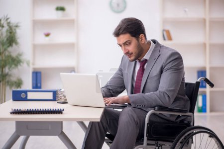 Photo for Young male employee in wheel-chair working at workplace - Royalty Free Image